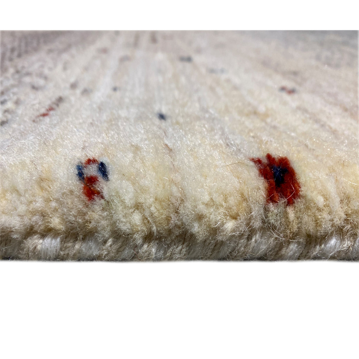Close-up of carpet pile: beige pile with individual red and blue/dark accents
