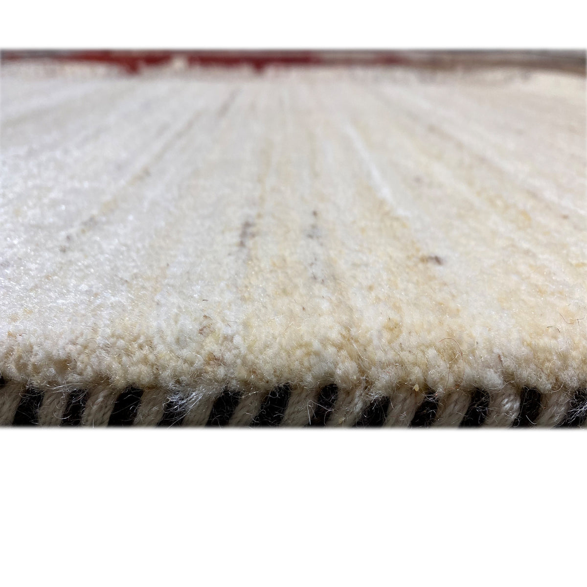 Close-up of the edge of a Gabbeh rug with short pile and contrasting black/red spots
