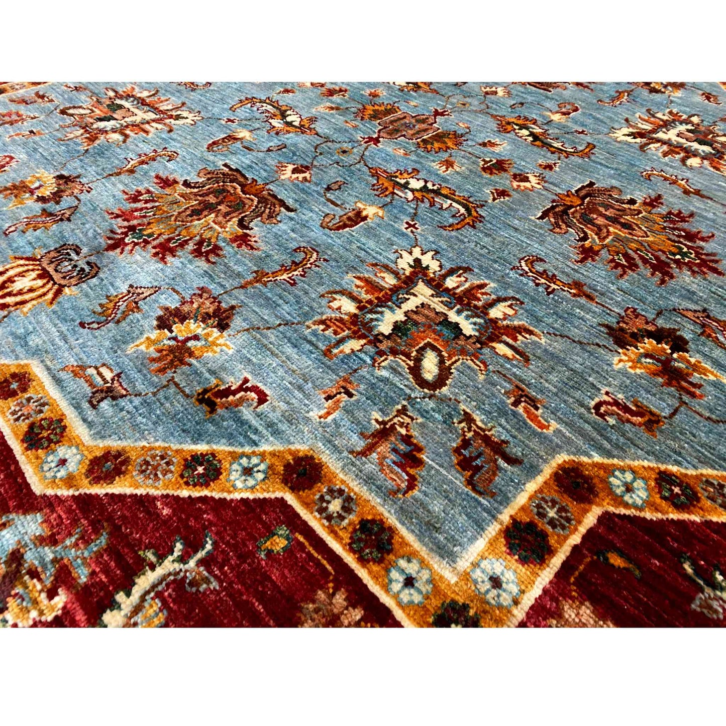 Close-up of a carpet pattern: light blue background with rust-colored and gold ornaments