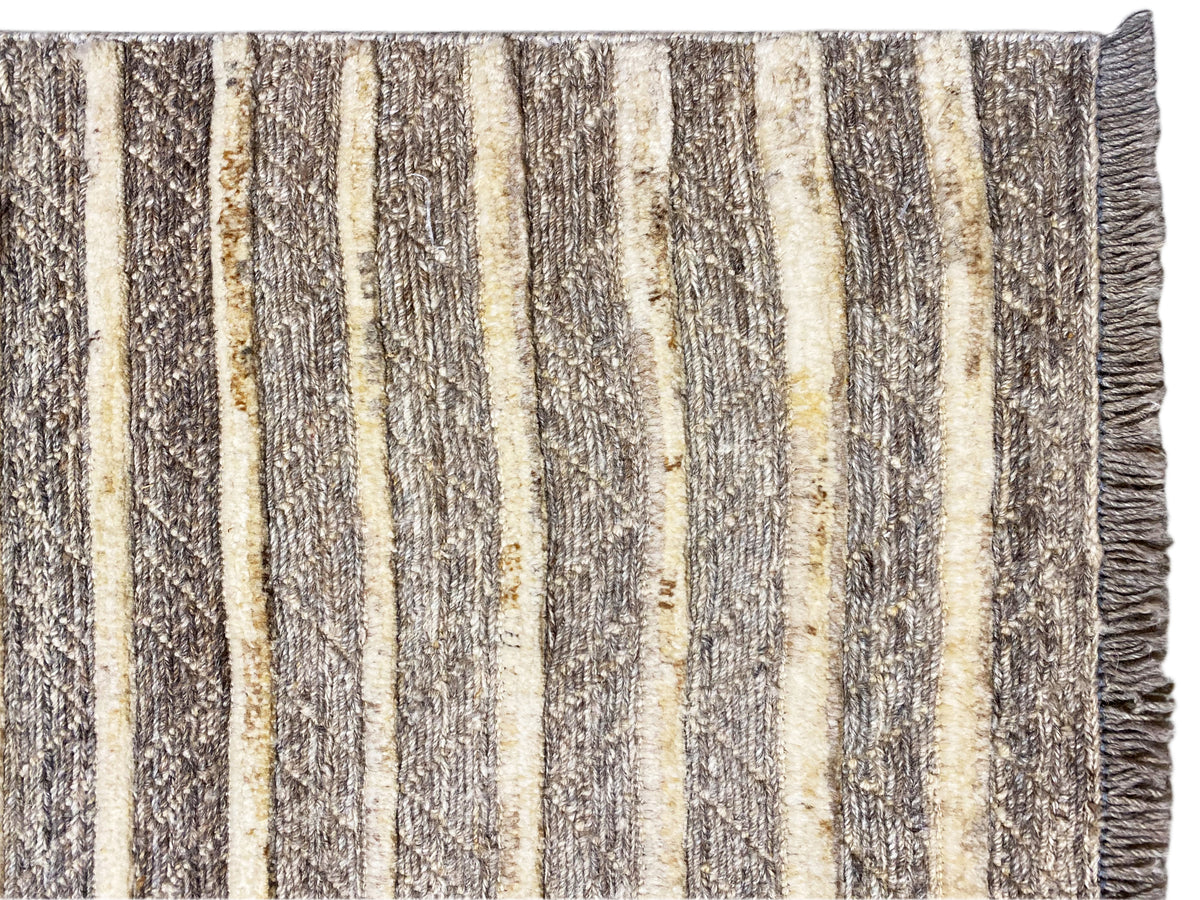 Nahaufnahme vom Kelim-Teppich: senkrechte Streifen in Beige, Grau und Gelb, fransiger Rand