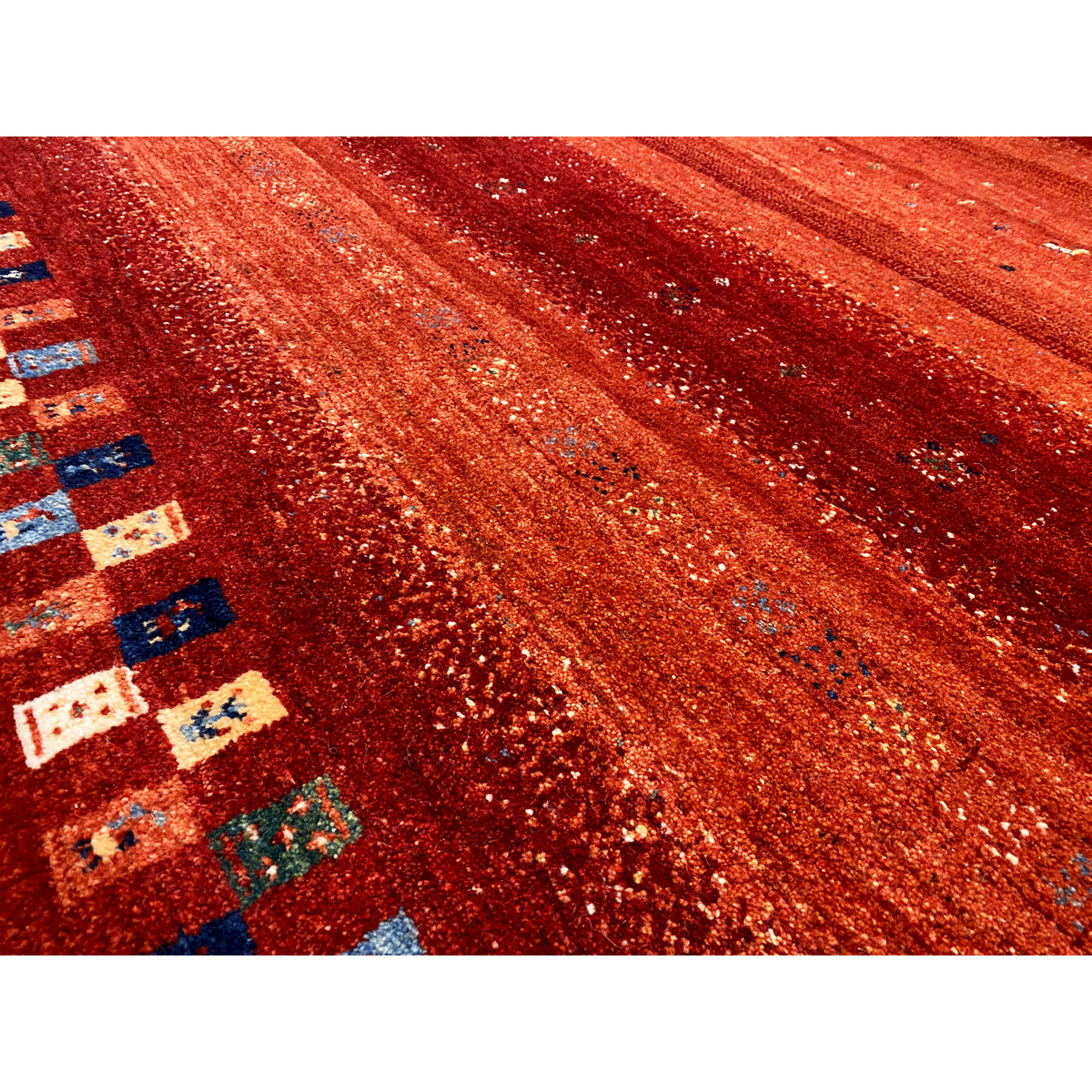 Close-up of a Gabbeh rug: reddish texture with a glitter effect and part of the multicolored border