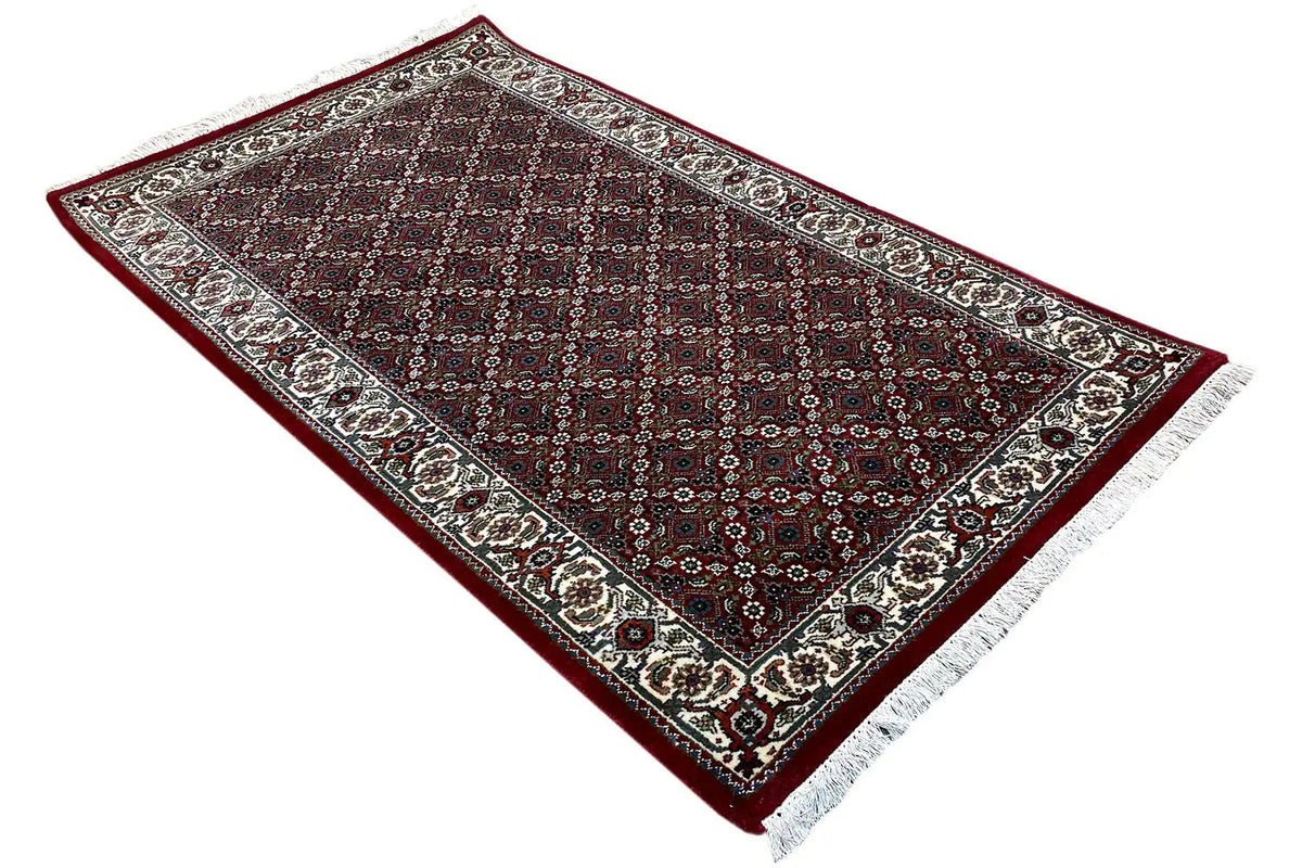 Bidjar rug at an angle: border around the edge, dark central field, short fringe at the corner