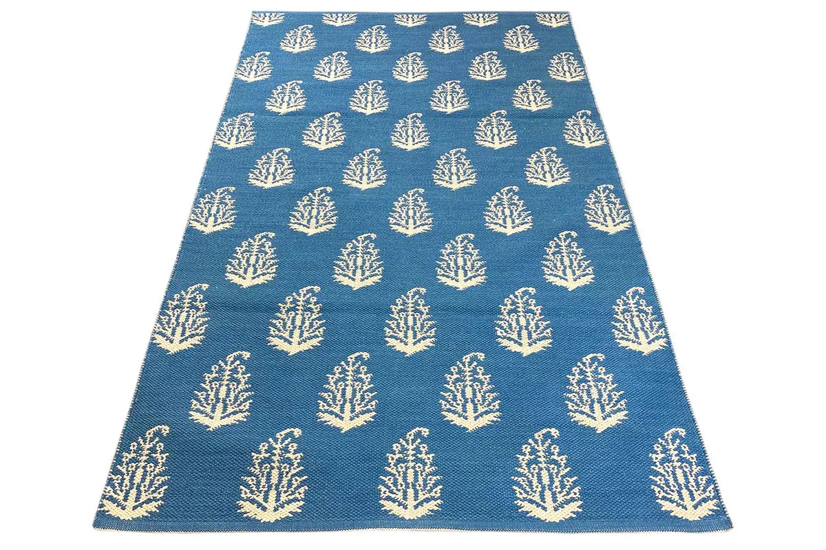 Blue A-shaped kilim rug with repeated tree/branch motifs in cream.