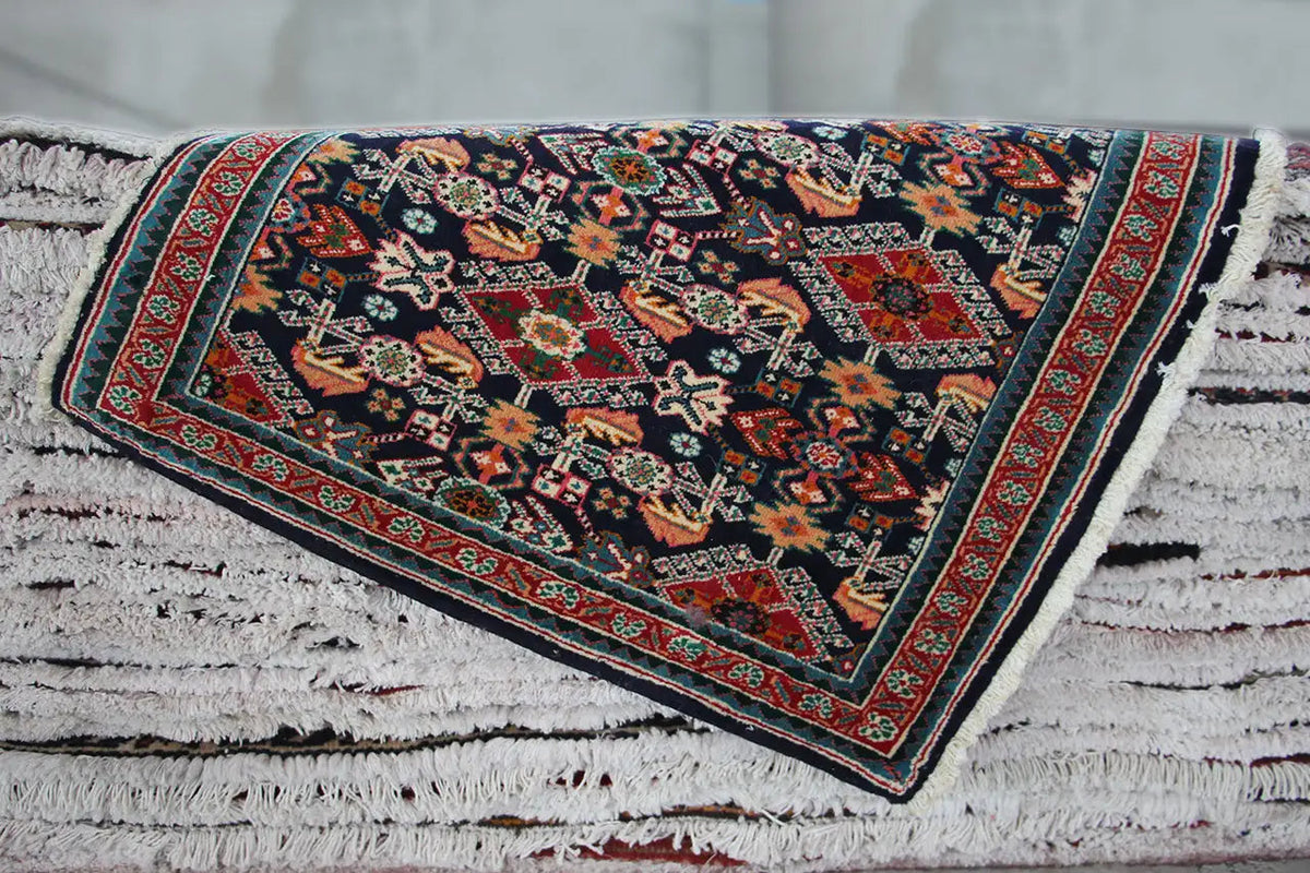Rectangular Oriental rug with a dark blue pattern, red border, and fringes