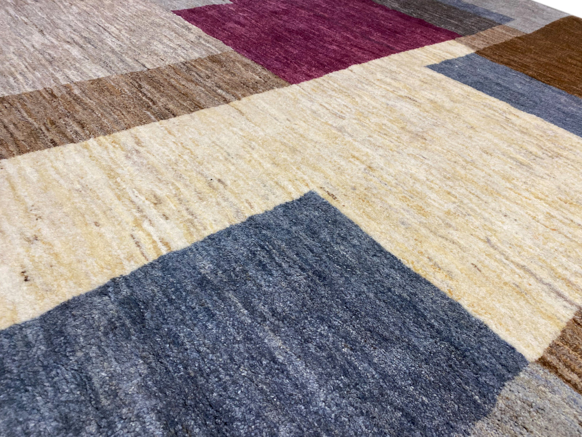 Detail vom Gabbeh-Teppich: leuchtendes creme, bordeauxes und blaues Blockfeld, gewebte Textur