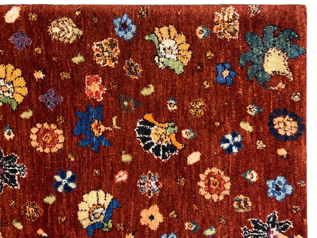 Teppich-Detailaufnahme: dichter Flor mit rötlich-braunem Grund und bunten Blumenmotiven.