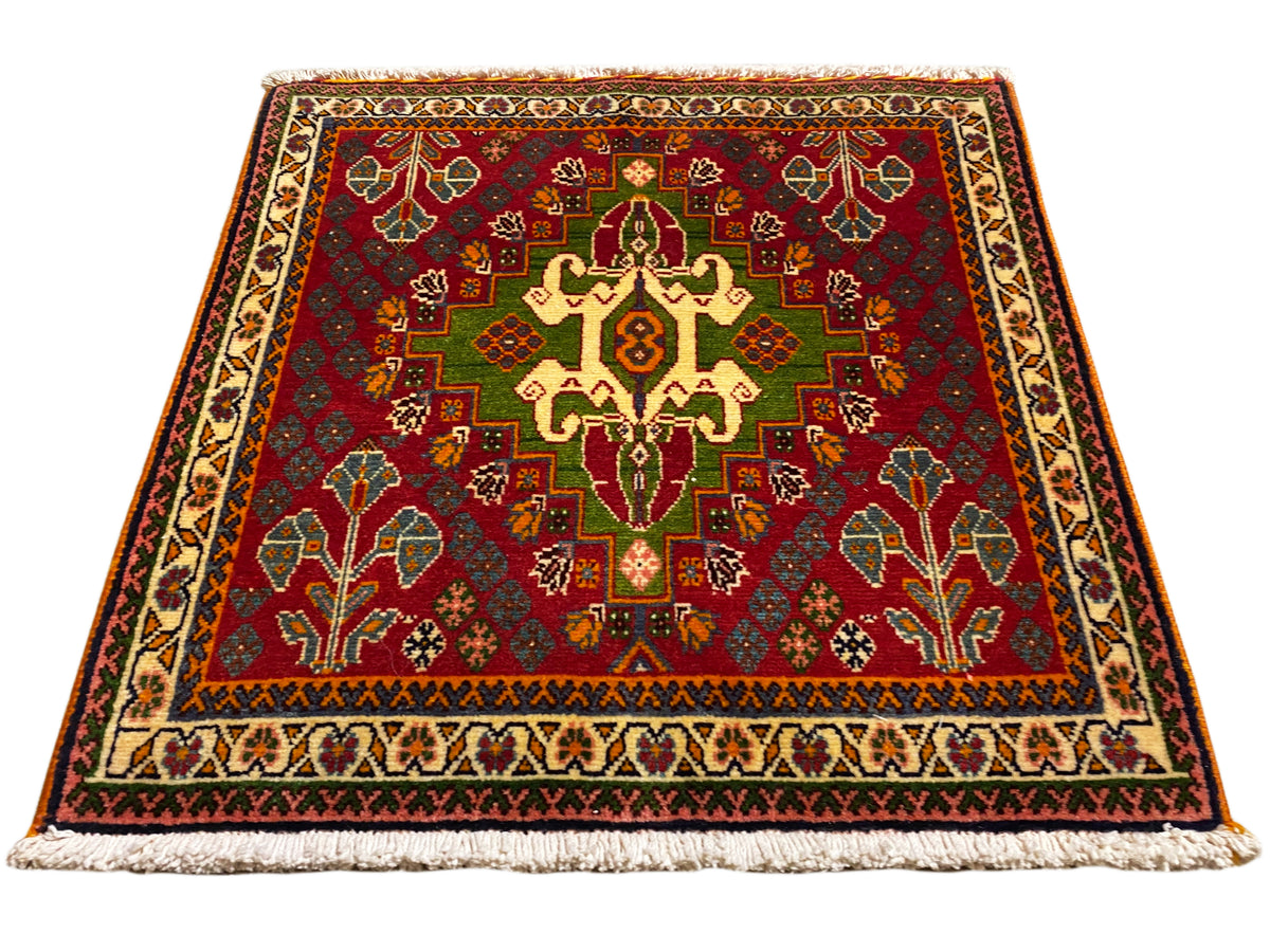Oriental rug with a red central motif, green details, and a beige border, with fringe