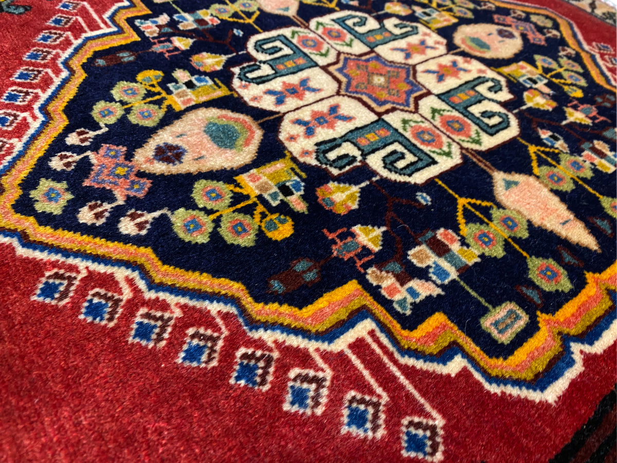 Poshti rug with a dark blue center, red borders, and colorful geometric motifs