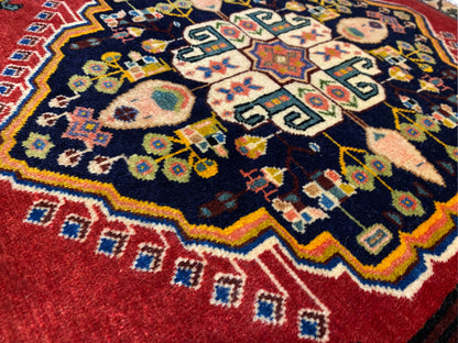 Poshti rug with a dark blue center, red borders, and colorful geometric motifs