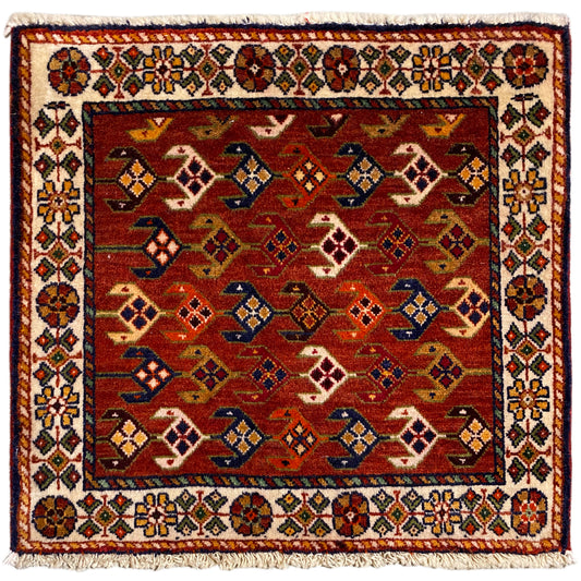 Square rug with a red background, a colorful white border, and fringes