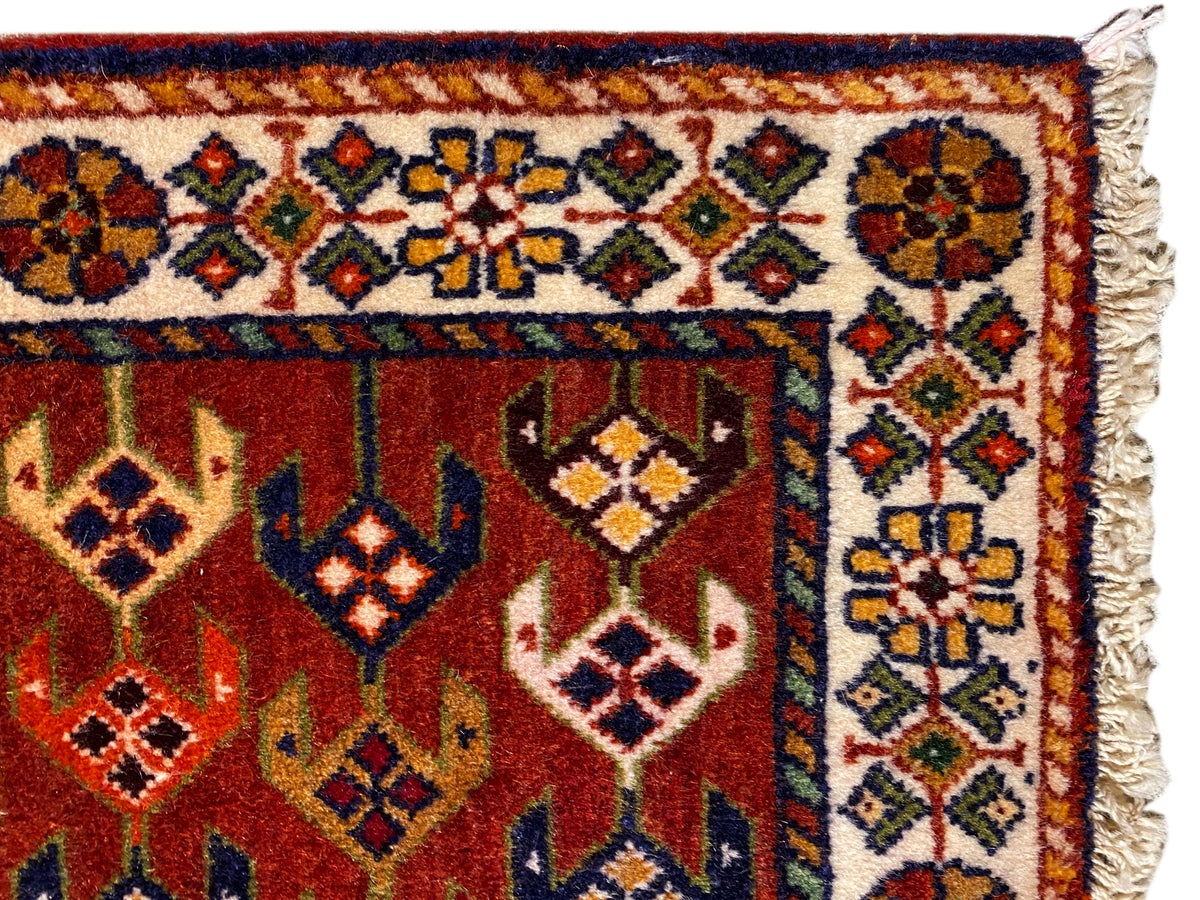 Carpet detail: red area with an ornamental border, colorful diamonds, and frayed side edges