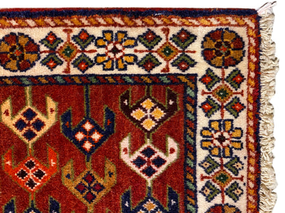Carpet detail: red area with an ornamental border, colorful diamonds, and frayed side edges