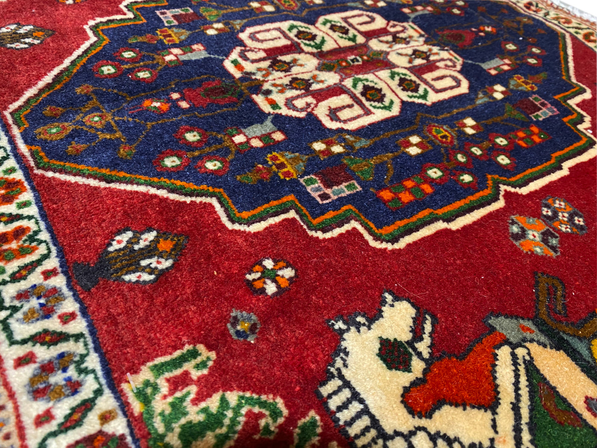 Close-up of a Poshti rug, red field with a blue ornamental wreath and animal motifs