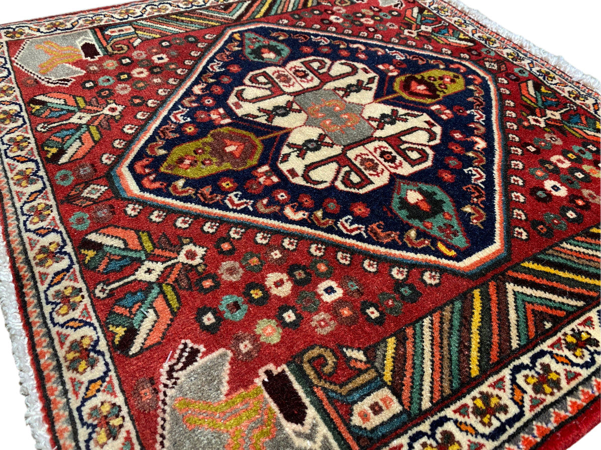Oriental rug photographed at an angle: red pattern, dark medallion, and multicolored borders
