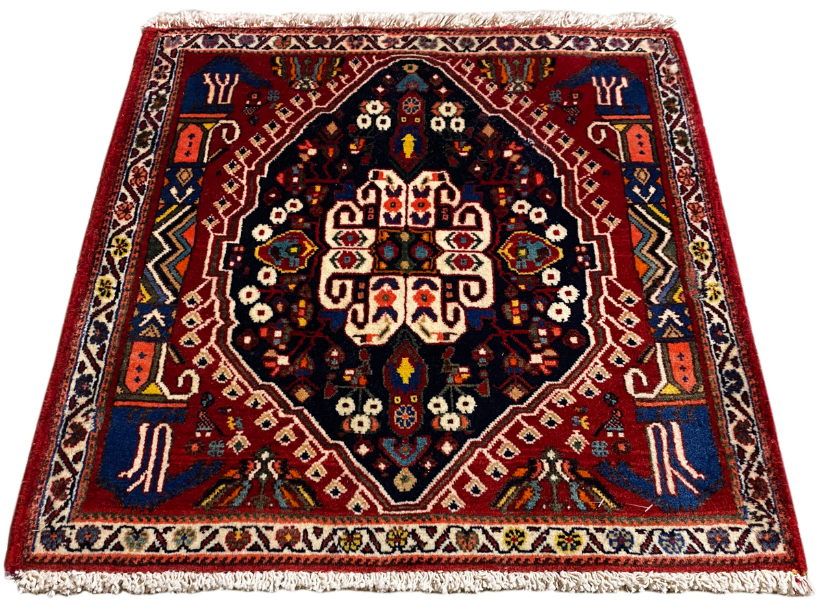 Rug with a red border, dark blue center, multicolored ornaments, and fringe