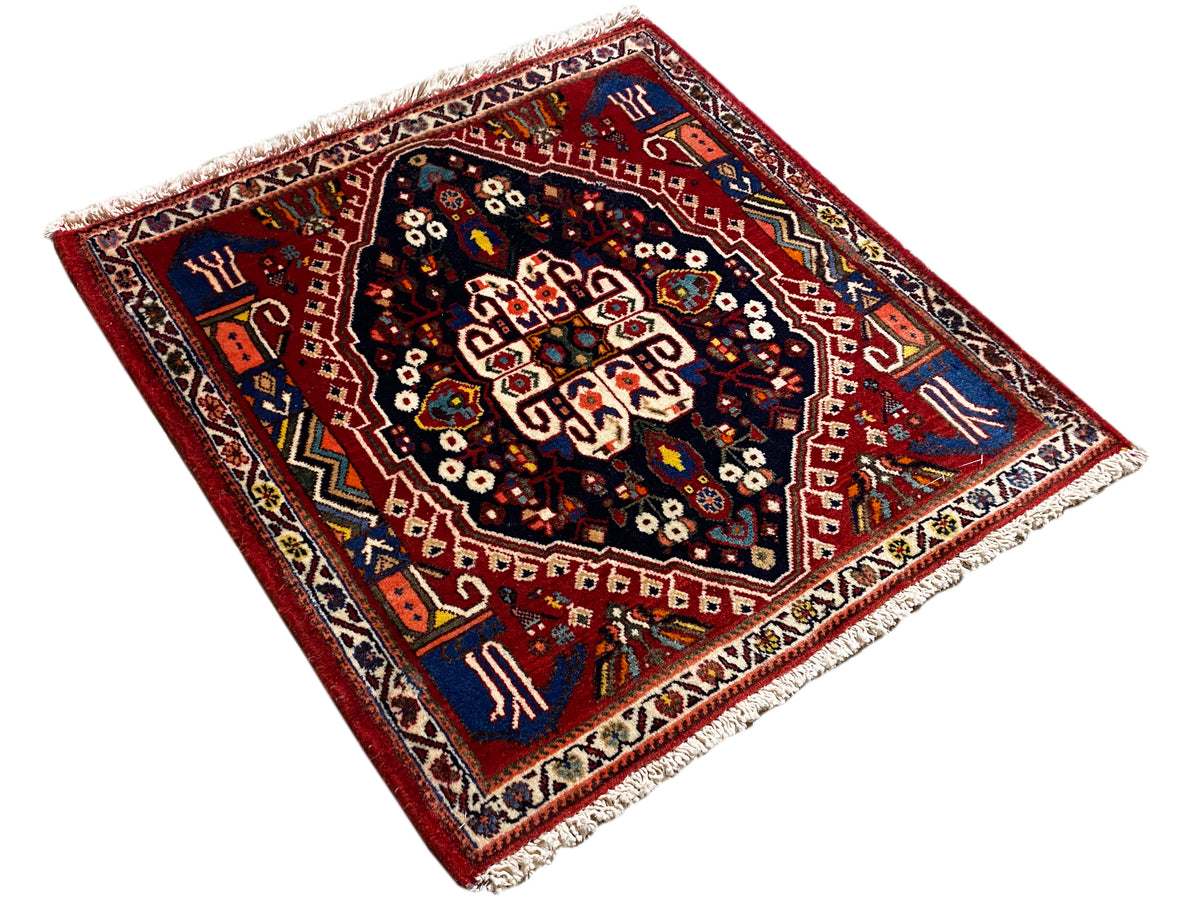 Nearly square-looking rug with a red ground, dark blue central medallion, and fringes